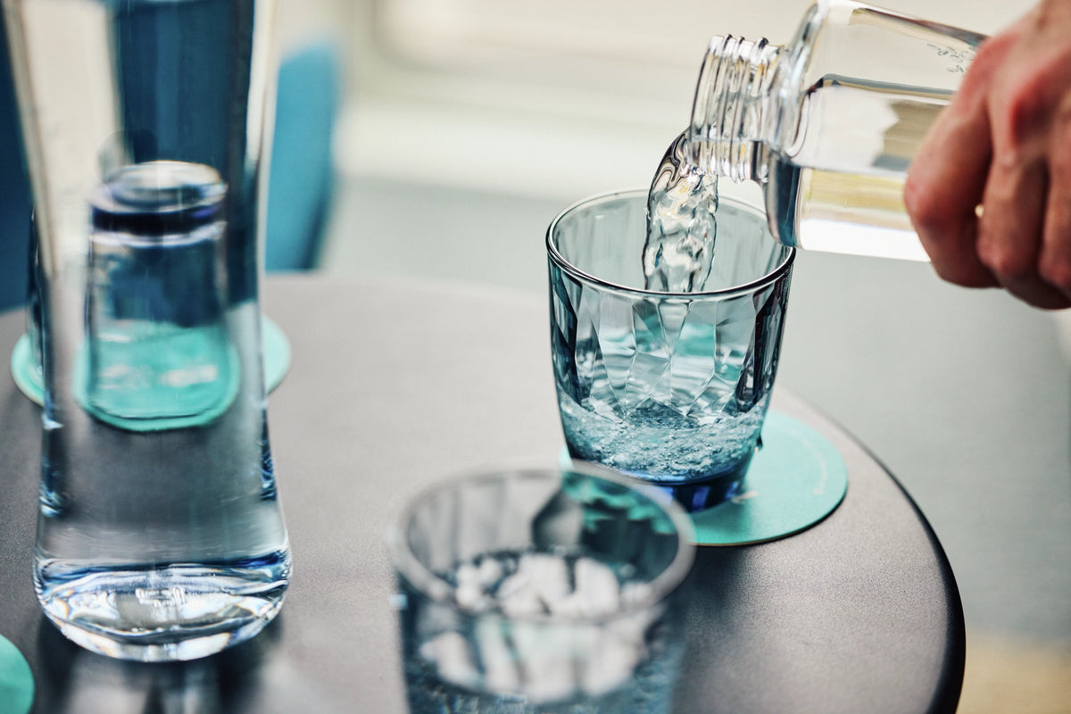 Person pouring water from a bottle into a glass on a table